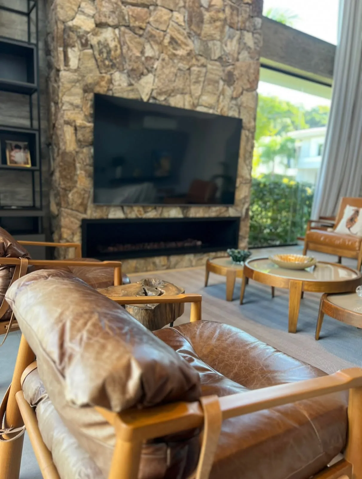 Living com lareira em pedra, poltronas de couro e integração ao jardim